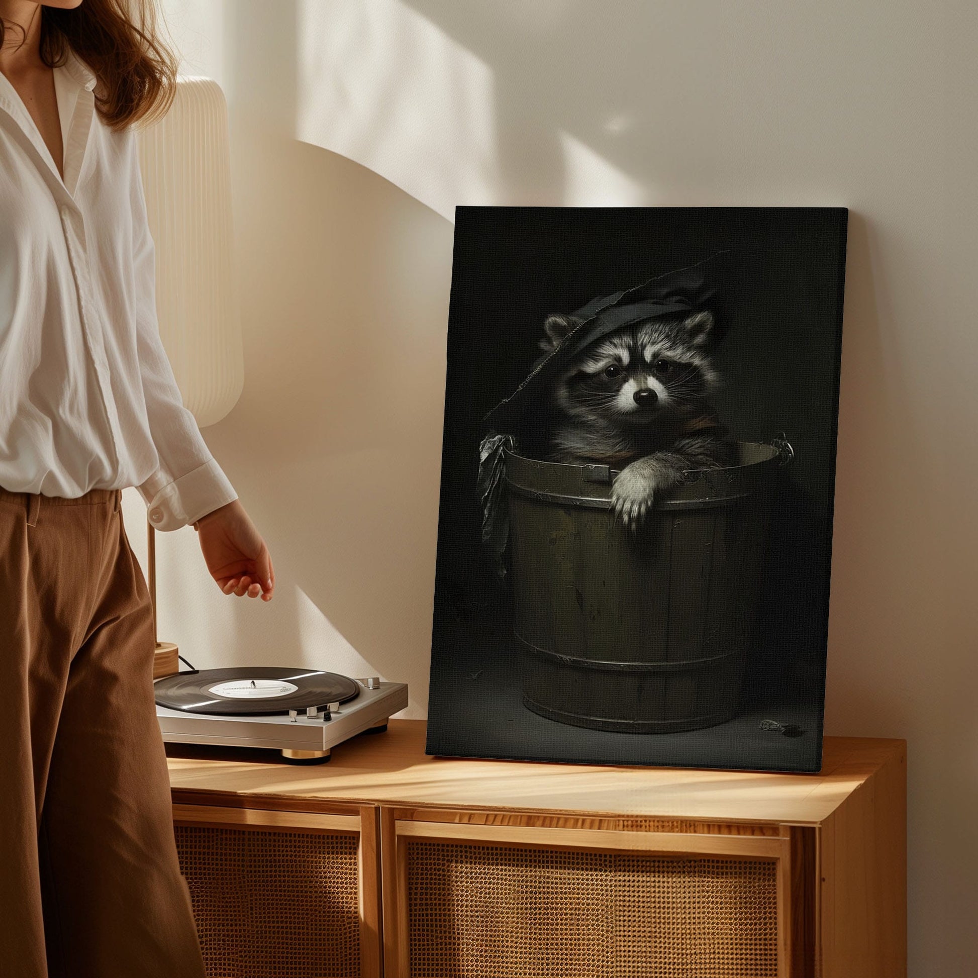 Trash panda canvas wall art featuring a raccoon sitting in a wooden bucket wearing a worn hat in moody dark vintage style