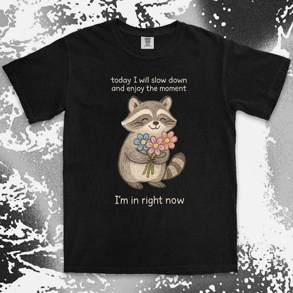 Comfort Color t-shirt with a smiling raccoon holding flowers and text ÒToday I will slow down and enjoy the moment Ð IÕm in right nowÓ in a soft, mindful design.