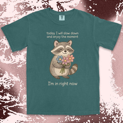 Comfort Color t-shirt with a smiling raccoon holding flowers and text ÒToday I will slow down and enjoy the moment Ð IÕm in right nowÓ in a soft, mindful design.