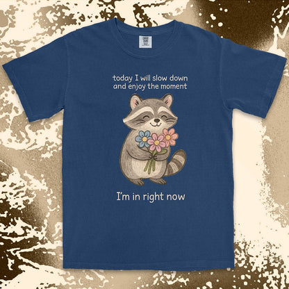 Comfort Color t-shirt with a smiling raccoon holding flowers and text ÒToday I will slow down and enjoy the moment Ð IÕm in right nowÓ in a soft, mindful design.